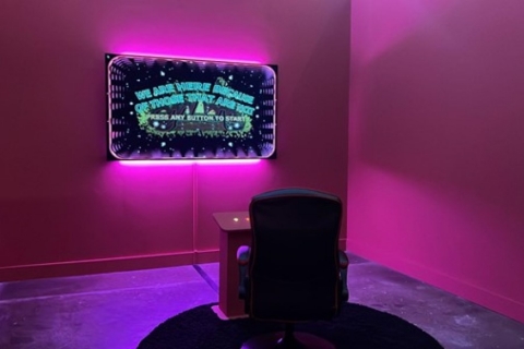A chair at a control panel in front of a screen, in a pink room