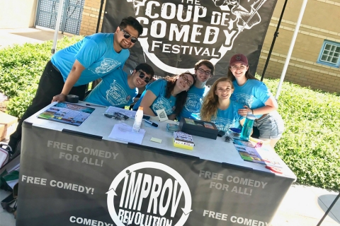 Smiling people in blue t-shirts sitting behind a table at a booth at a fair