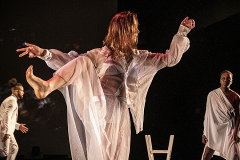 red headed girl dressed in all white dancing with her right leg held high at an angle.  