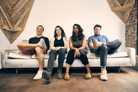 Four people sitting on couch in a room with brick and wood accents on walls