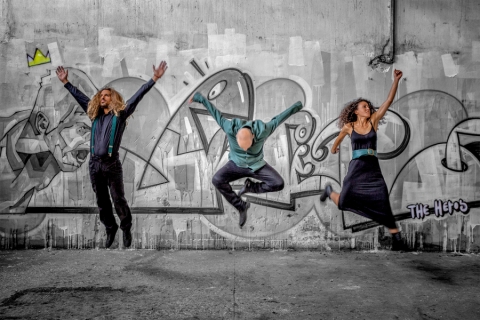 Members of the Galan Trio jumping in front of a graffitied wall
