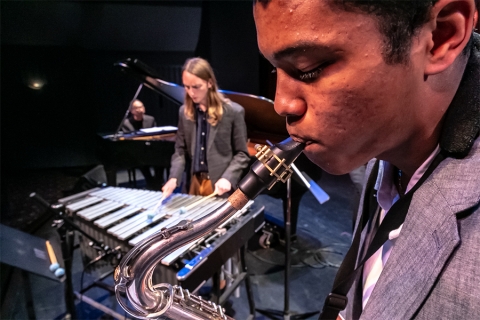 Image of saxophone player in foreground; xylophone player behind; Kei Akagi at piano in background