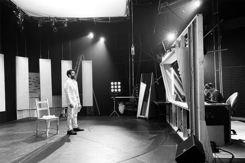 Man in white under lights of a sound studio, a technician on the other side of a glass partition