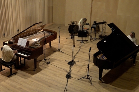 Musicians in a sound studio with 2 pianos, a drumset, and electronics