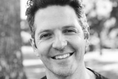 Black and white photo closeup of smiling man in a park, a tree in the background