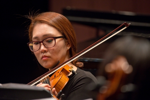 A woman in glasses holds a violin to her chin with bow midair
