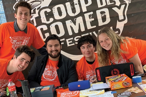 Smiling people in orange t-shirts sitting behind a table at a booth at a fair