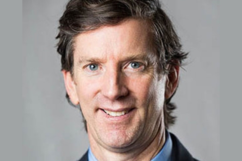 Closeup of smiling man with dark hair and blue eyes, wearing a suit