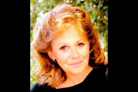 Smiling woman with red hair, in front of greenery