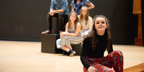 Young actors on stage, sitting, smiling toward what would be the skyline for them