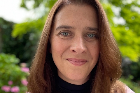 Headshot of smiling woman with brown hair in front of greenery and flowers